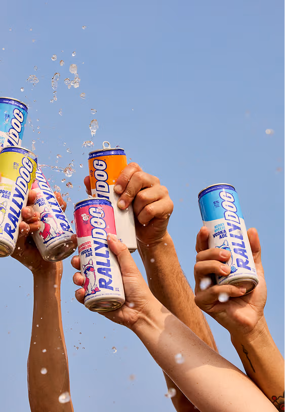 Several hands cheersing with cans of Rally Dog Vodka Ade