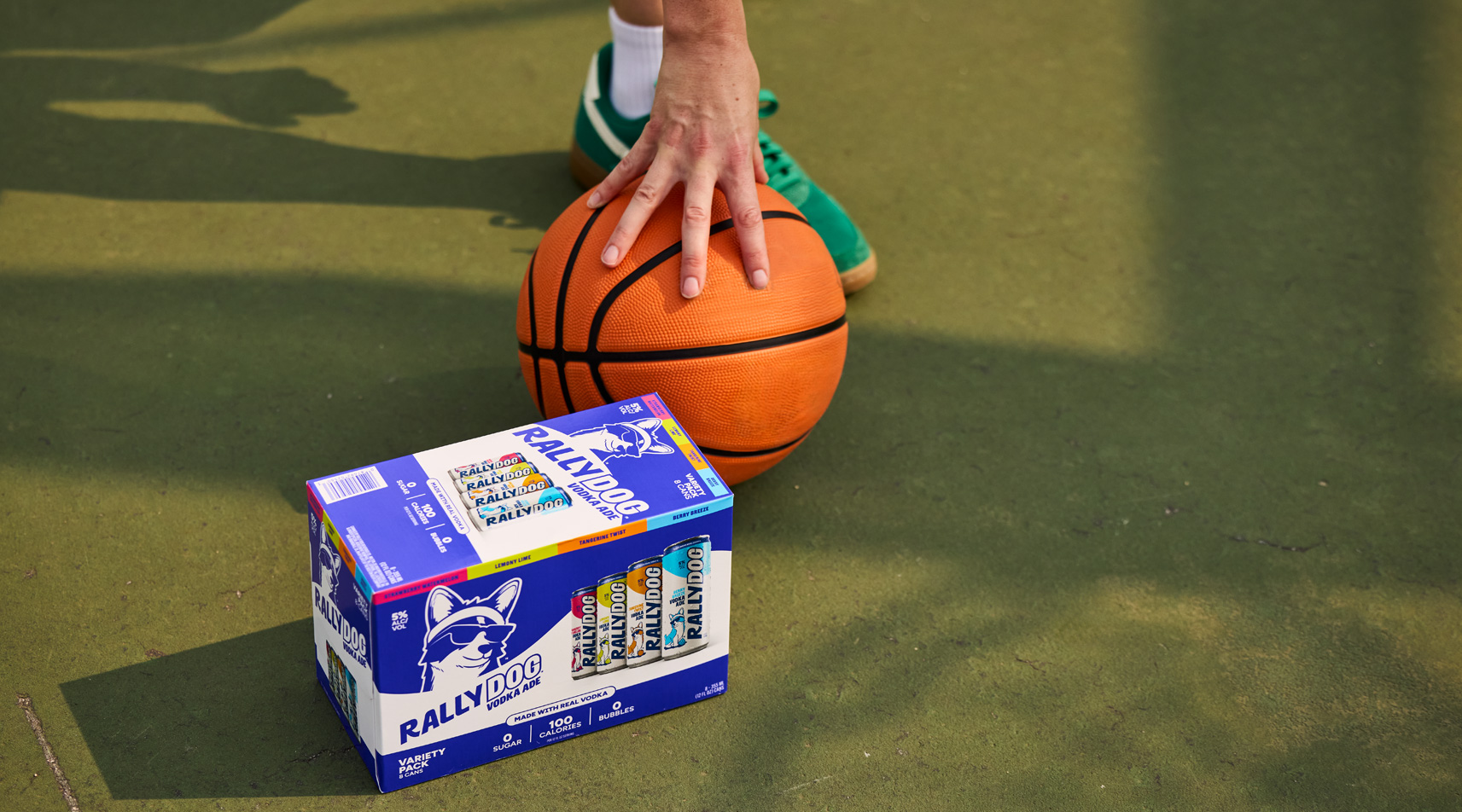 A hand touching a basketball from above with a variety pack of Rally Dog in the foreground.