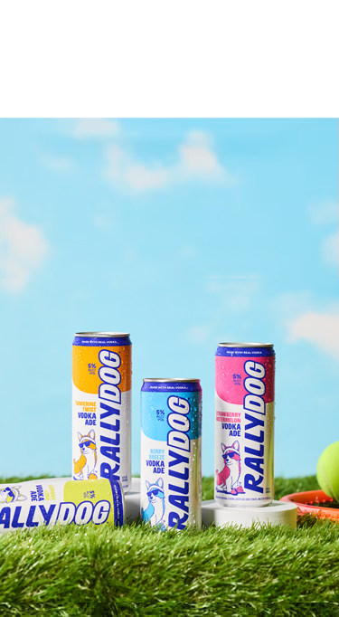 a few cans of Rally dog sitting on grass with a bluesky above and a tennis racket and ball next to it